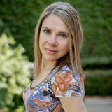 Portrait of Dr. Terry Ann smiling in a patterned top against a lush green outdoor background.