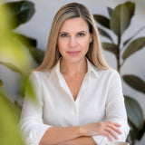 Professional portrait of Dr. Terry Ann wearing a white button-down shirt with arms crossed in front of green plants.