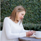 Dr. Terry Ann sitting outdoors at a table writing in a journal next to a coffee mug.