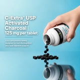 Black activated charcoal tablets pouring from the Naturmade Charco Tabs 120s bottle onto a reflective surface.
