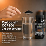 A spoon holding fine black activated charcoal powder over a glass of water next to the Naturmade Charco-Max bottle.