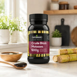 Naturmade Crude Black Molasses 500g bottle on a kitchen counter with raw sugarcane stalks and molasses in a wooden spoon